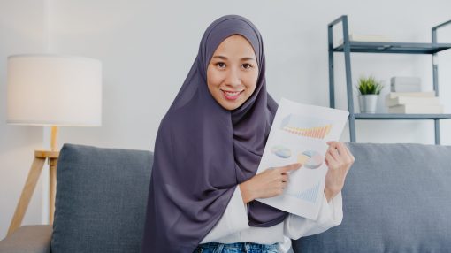 Asia muslim lady wear hijab use computer laptop talk to colleagues about sale report in video call meeting while remotely work from home at living room. Social distancing, quarantine for corona virus.